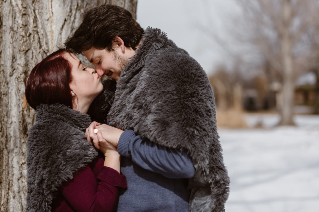 Woman kissing fiancé's nose while wrapped in a fuzzy blanket