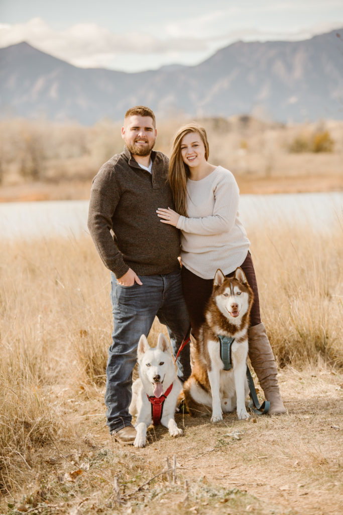 Couple standing next to each other smiling with their two huskies