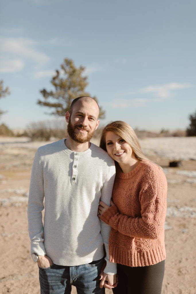 Woman holding fiancé's arm both smiling and looking at the camera