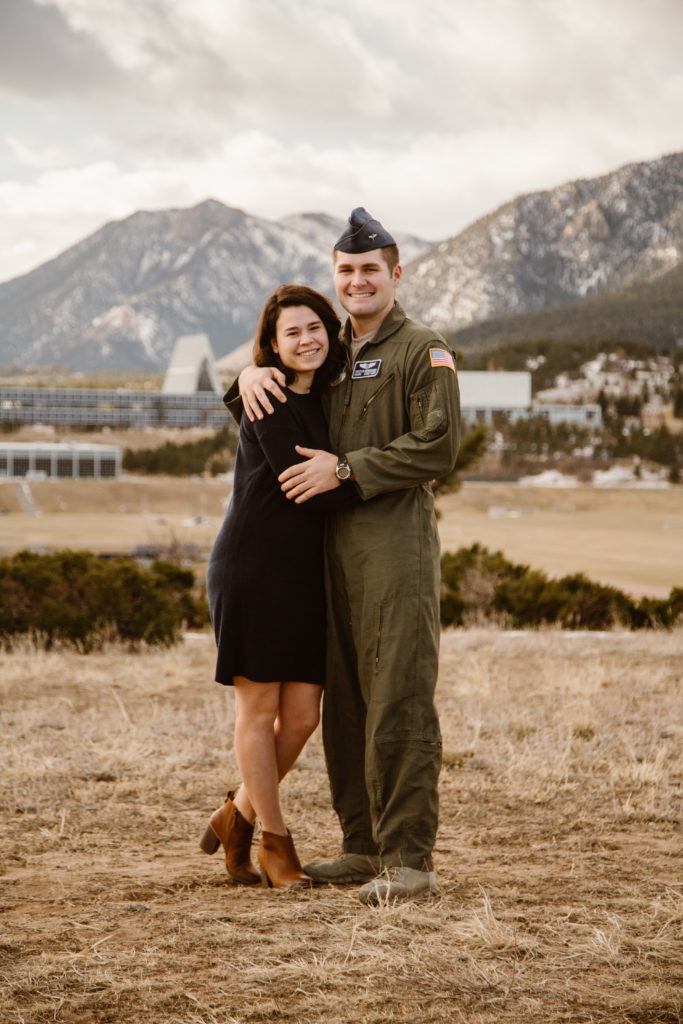 Man in Air Force uniform with is arms around his fiancé, both looking at the camera