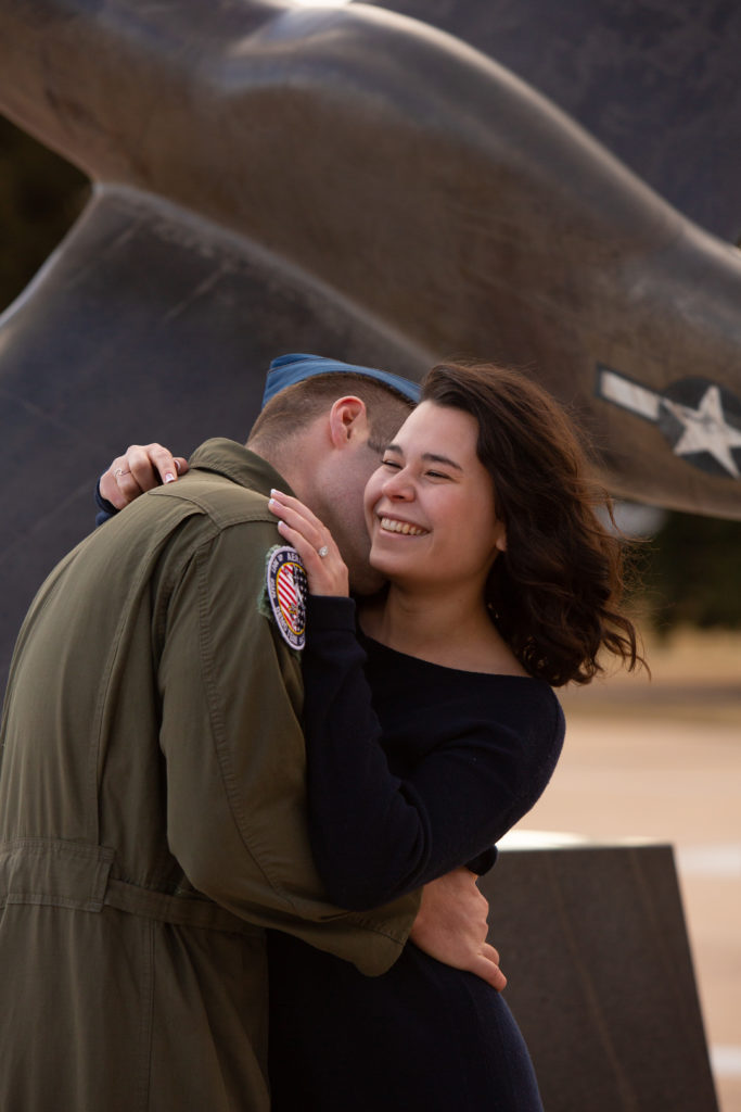 Man in Air Force uniform kissing his fiancé's neck as she smiles