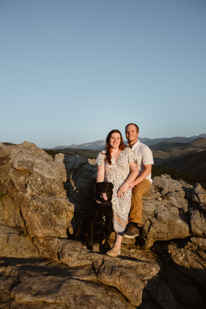 Couple sitting on a rock with their dog and smiling