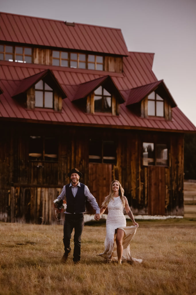 Bride and groom running in a field with a barn behind them