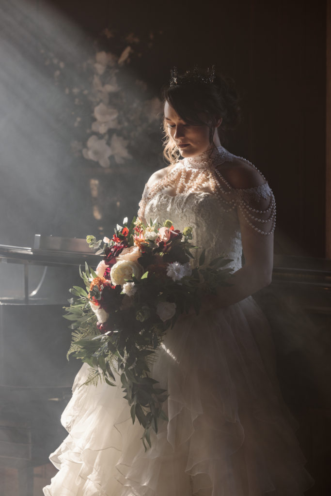 Portrait of a bride looking at her flowers in front of a piano with fog.