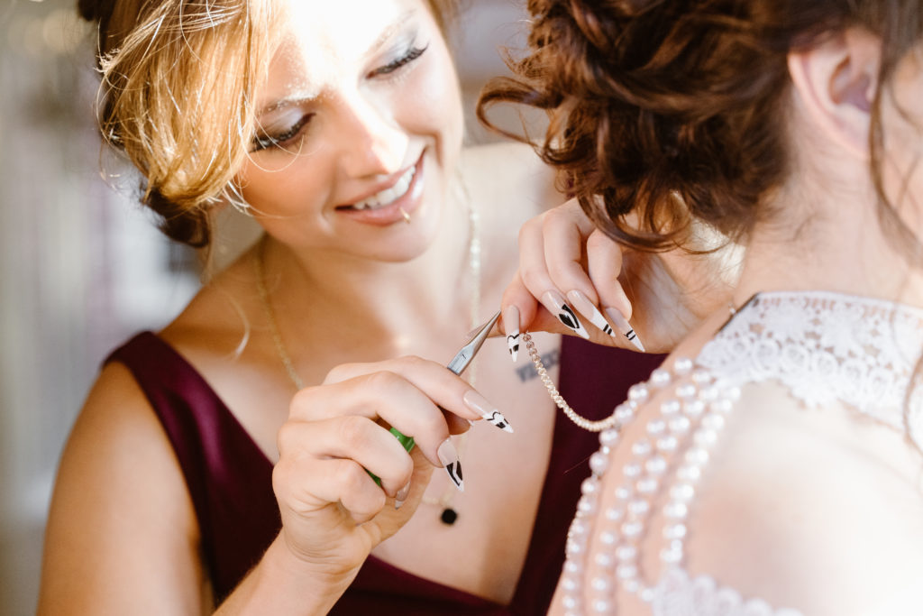 Bridesmaid fixing bride's jewelry.