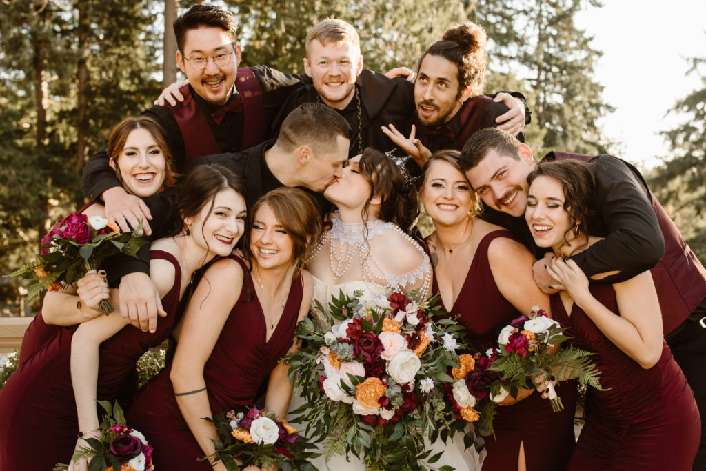 Whole bridal party with groom and bride kissing.