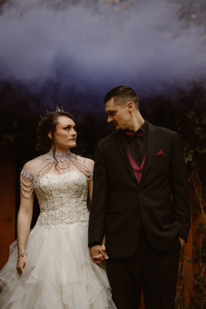 Bride and groom holding hands with colored smoke behind them.