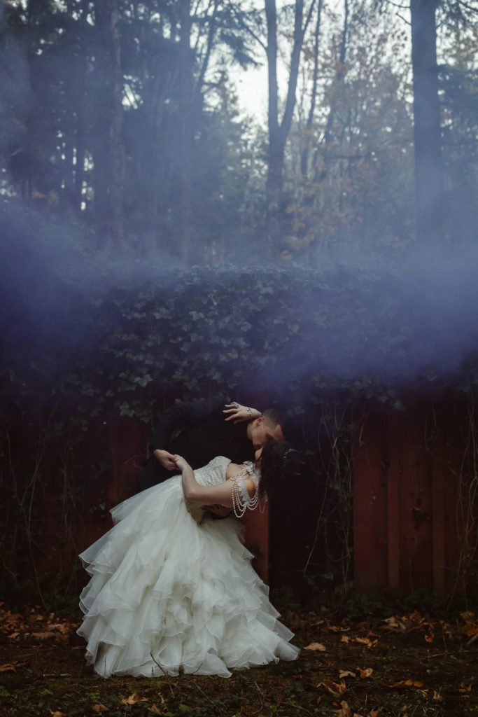 Bride and groom holding hands with colored smoke behind them.