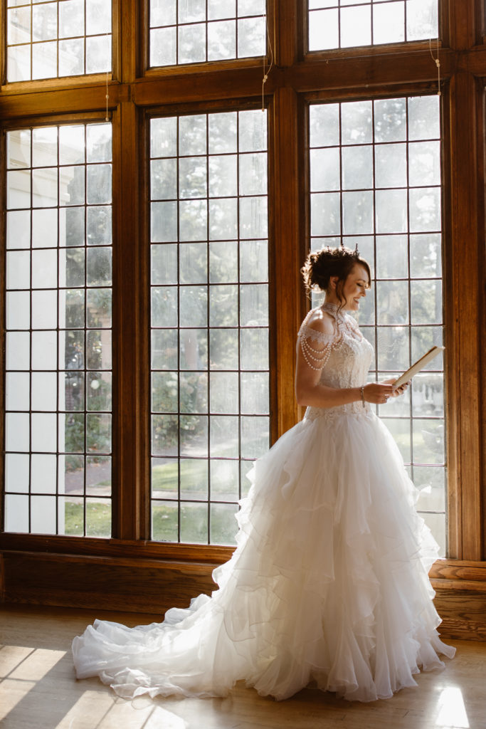 Portrait of a bride reviewing her vows in front of a wall of windows.