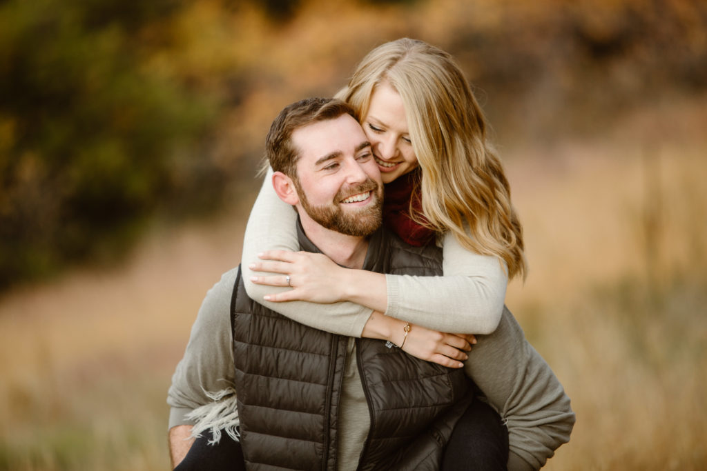Couple with a woman on a mans back, arms wrapped around him and they are both smiling