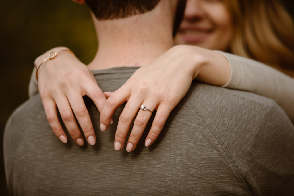 Woman's hands with an engagement ring on, hands are wrapped around man's neck