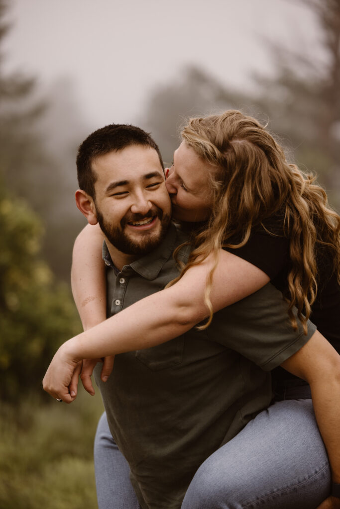 Woman on her fiancé's back giving him a kiss on the cheek