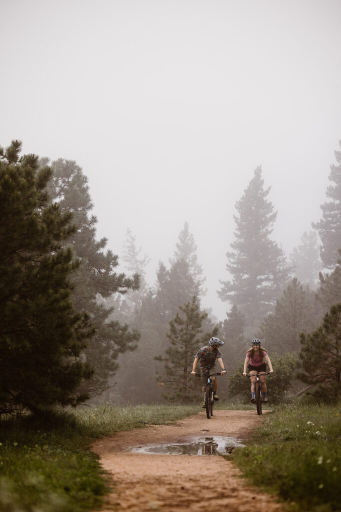 Engaged couple riding their mountain bikes on a dirt path. Man is looking back at his fiancé