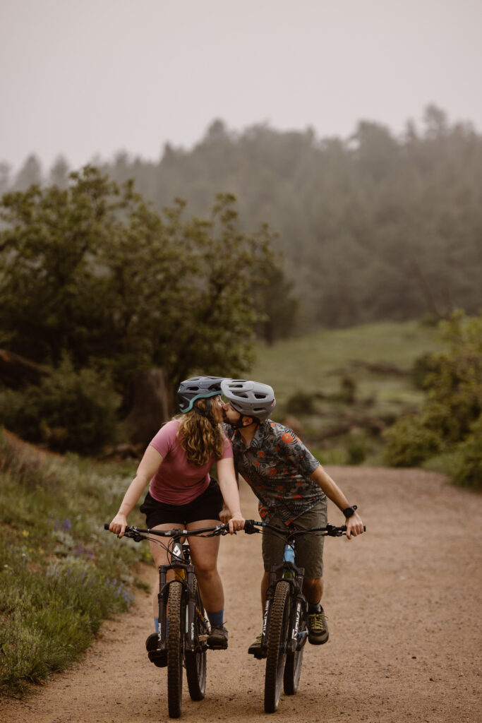 Engaged couple sharing a kiss while riding their mountain bikes on a dirt path