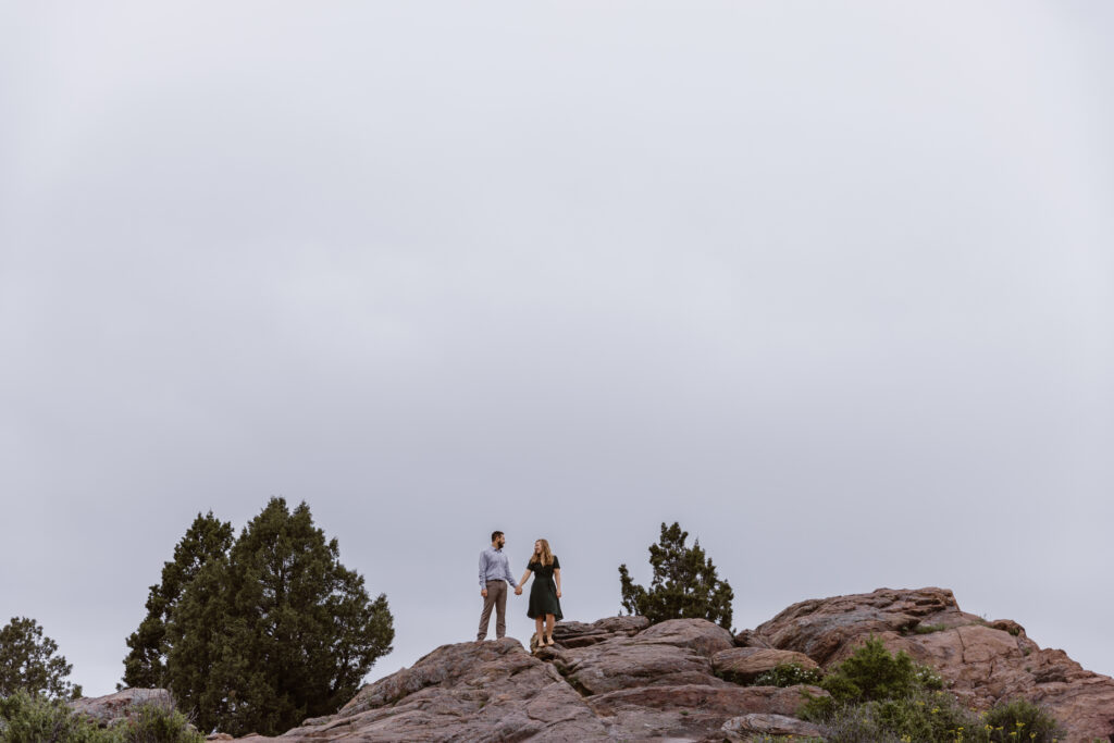 Engaged couple holding hands on top of a big rock