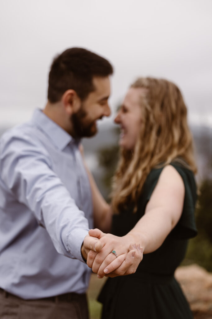 Engaged couple looking into each other's eyes smiling holding hands. Woman's hand is in focus highlighting her engagement ring