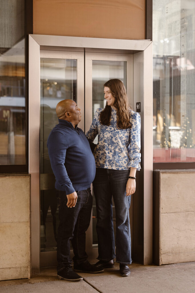 Couple standing in front of a glass elevator looking at each other