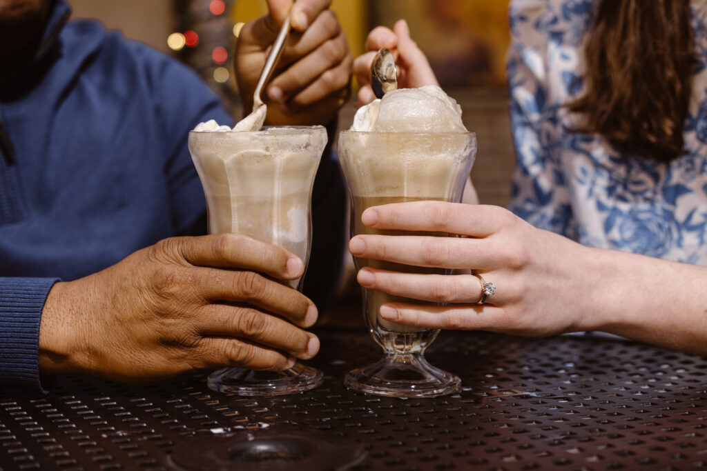 Couple's hands holding their glasses of root beer floats, highlighting woman's engagement ring