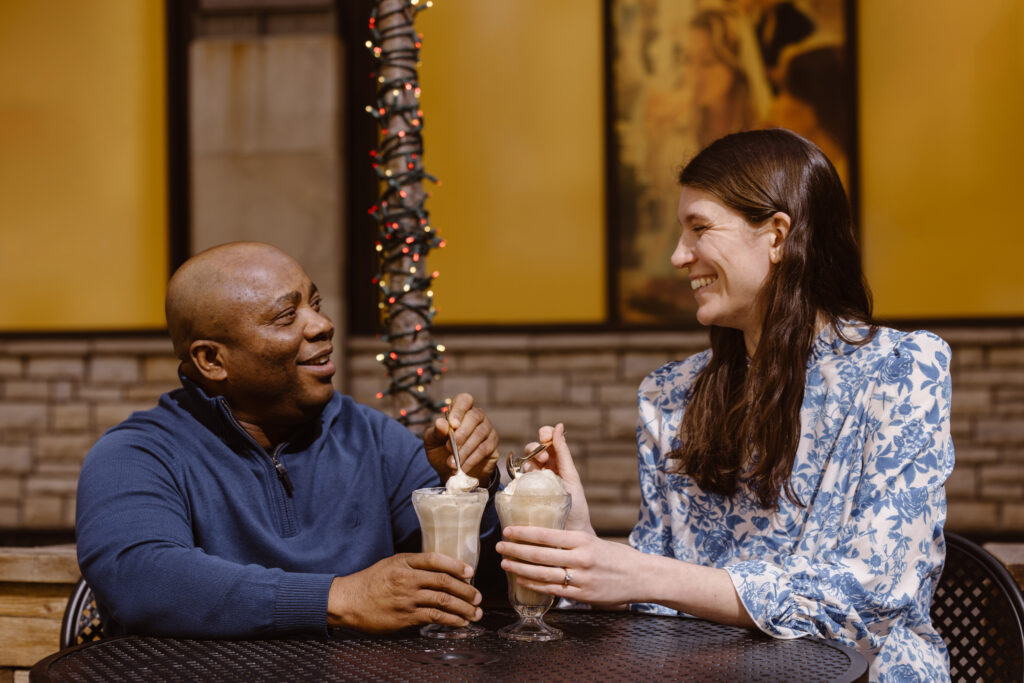 Couple smiling at each other while eating root beer floats at an outside table