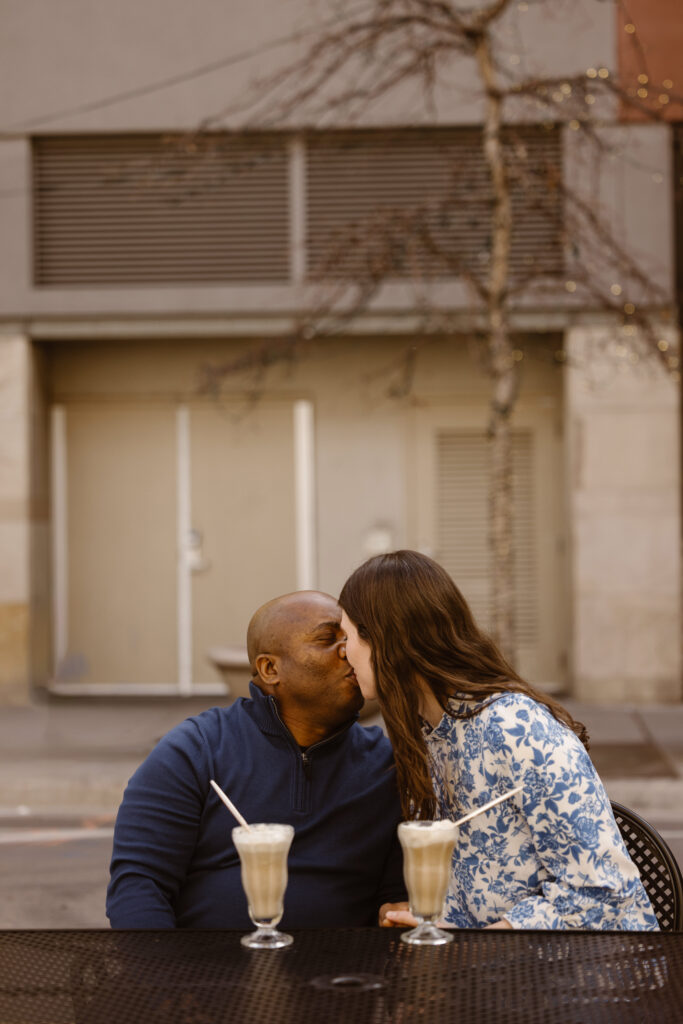 Couple sharing a kiss over root beer floats at an outside table