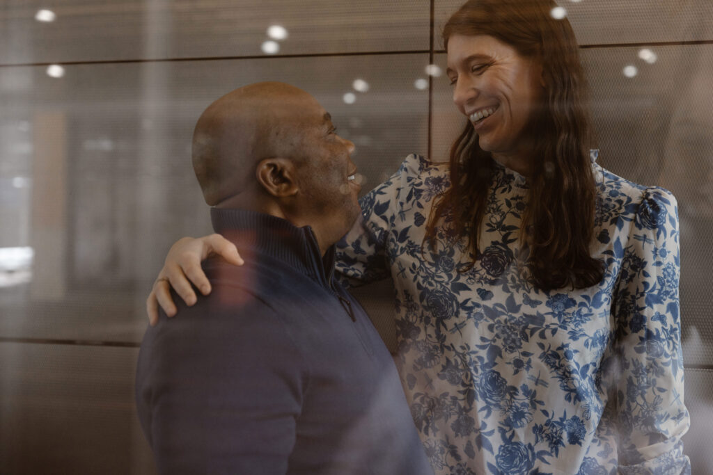 Couple inside a glass elevator looking at each other smiling