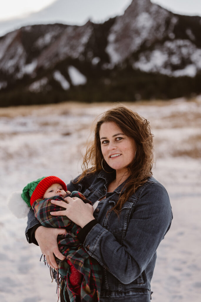 Mother holding her newborn daughter with snowy Flatirons in the background
