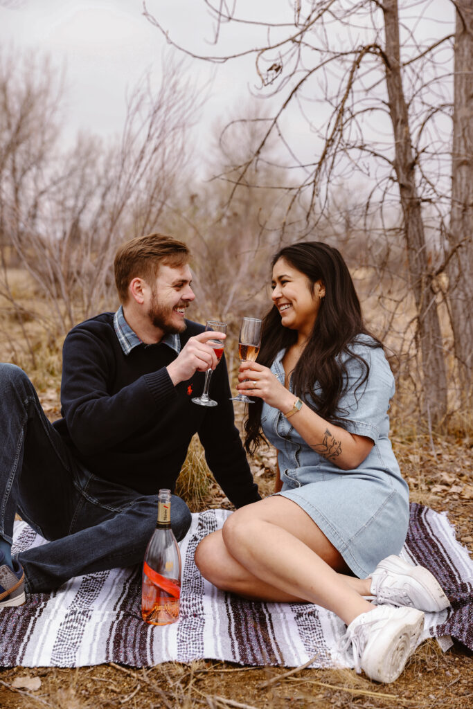 Engaged couple cheersing with champagne on a blanket