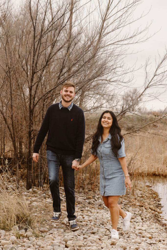 Couple walking hand in hand looking at each other smiling by a lake