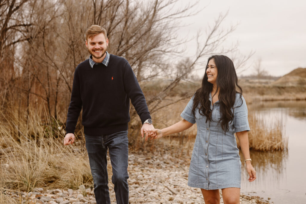 Couple walking hand in hand looking at each other smiling by a lake