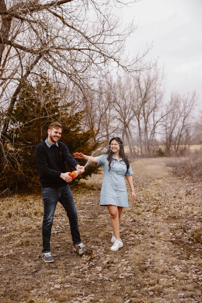 Man spraying bottle of champagne with his fiancé