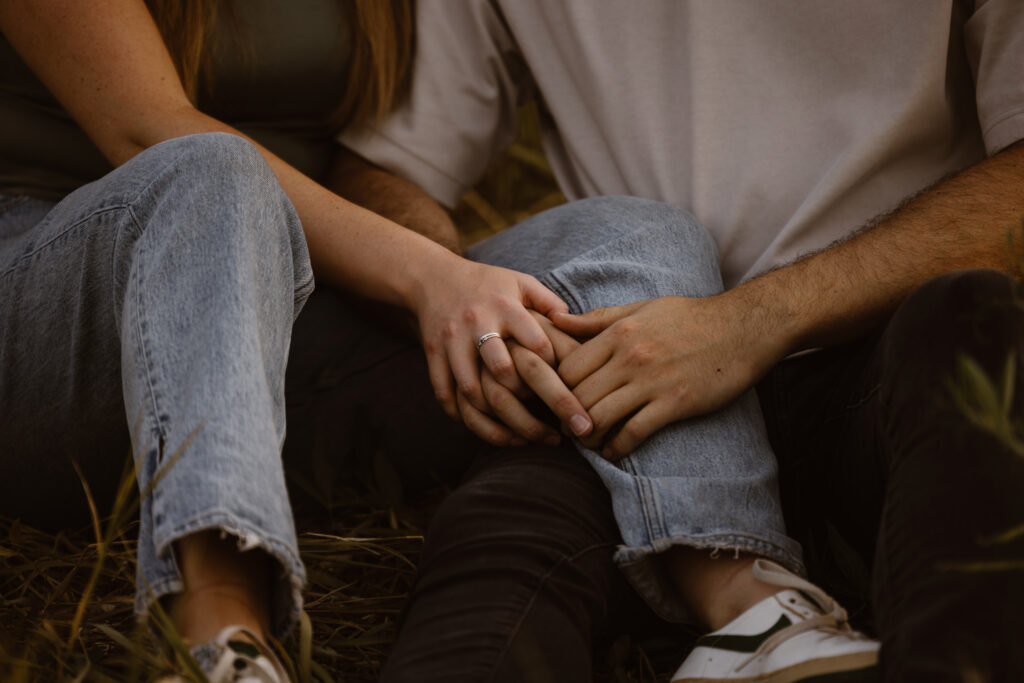 Close-up of an engaged couple holding hands in a field, showing the engagement ring during their Chautauqua Park engagement session in Boulder, Colorado.