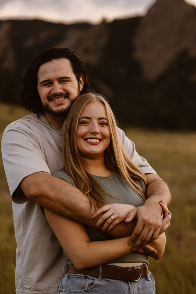 Smiling engaged couple embracing in front of the Flatirons in Boulder, Colorado during their engagement session.