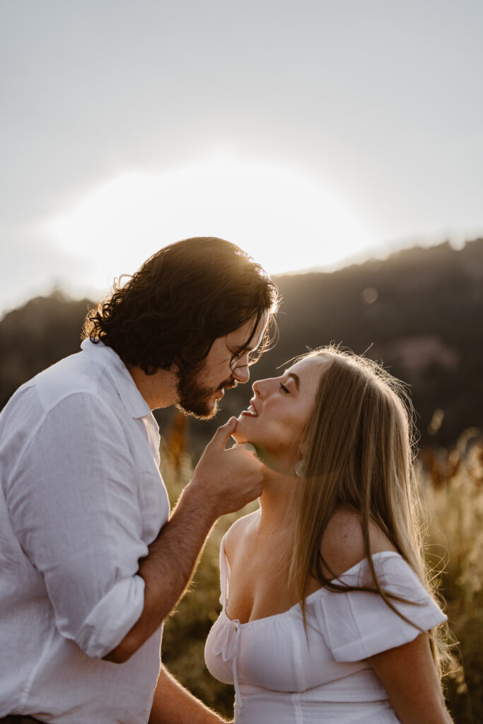 Groom-to-be gently holding his fiancée’s chin as they share an intimate moment during their Boulder engagement session at sunset.
