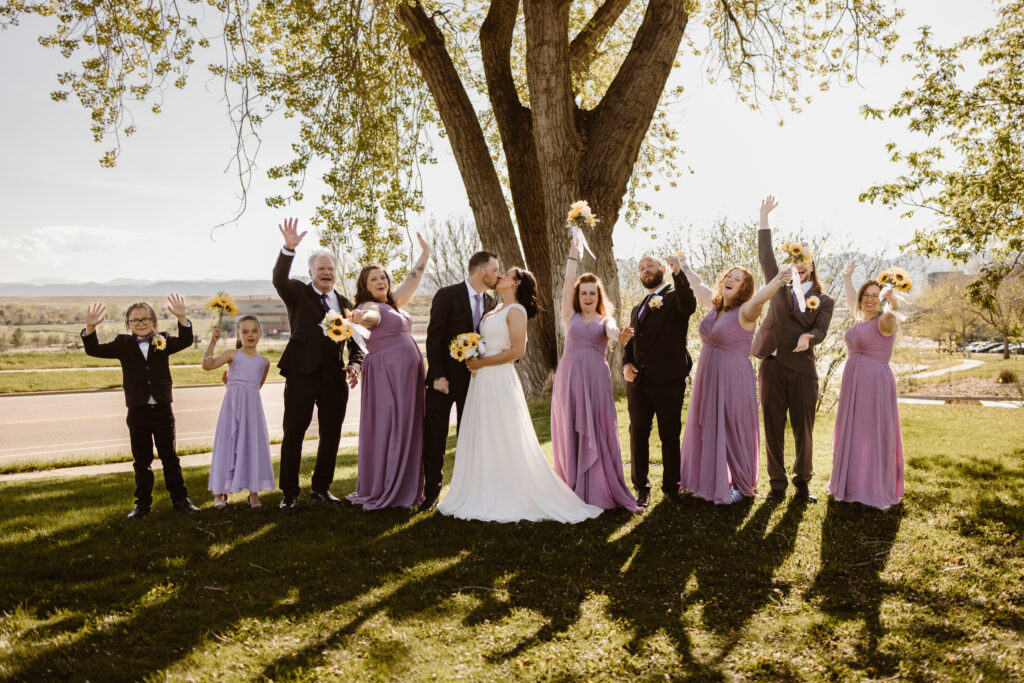 Bride and groom share a kiss with their bridal party celebrating all around them