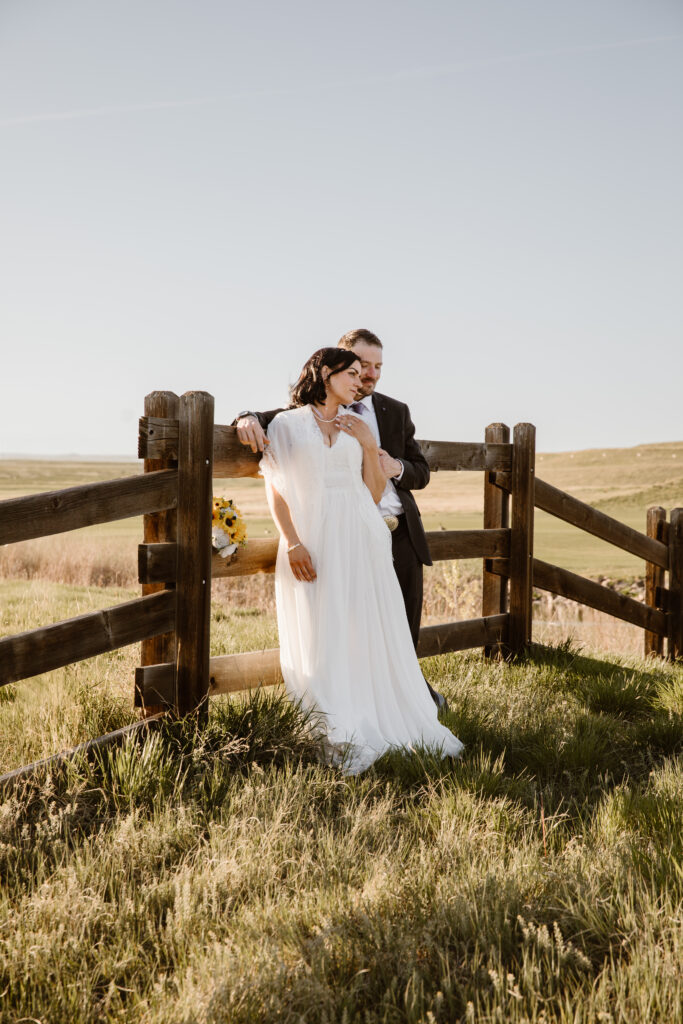 Bride and groom embracing by wooden fence at Walnut Creek Golf Preserve wedding in Westminster Colorado during golden hour by Colorado wedding photographer.